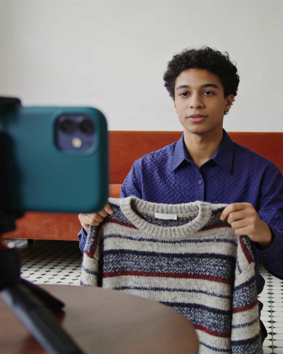 Kreator memperlihatkan sweter bergaris ke kamera HP di tripod
